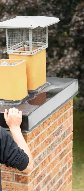 Technician steadying a chimney crown beside a stainless cap and clay flue tiles