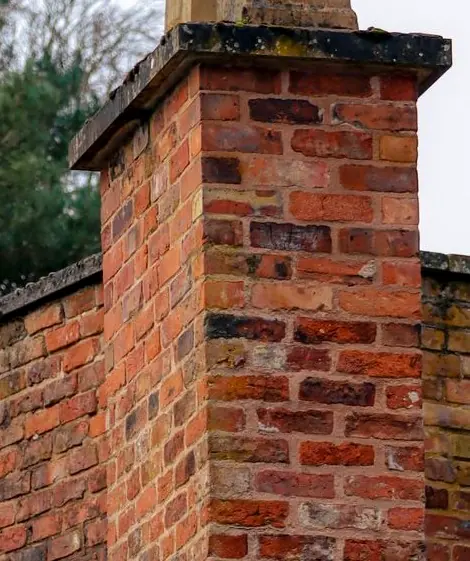 Weathered brick chimney stack with a deteriorating stone crown and failing mortar joints