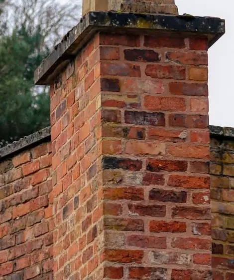 Weathered brick chimney stack with a deteriorating stone crown and failing mortar joints