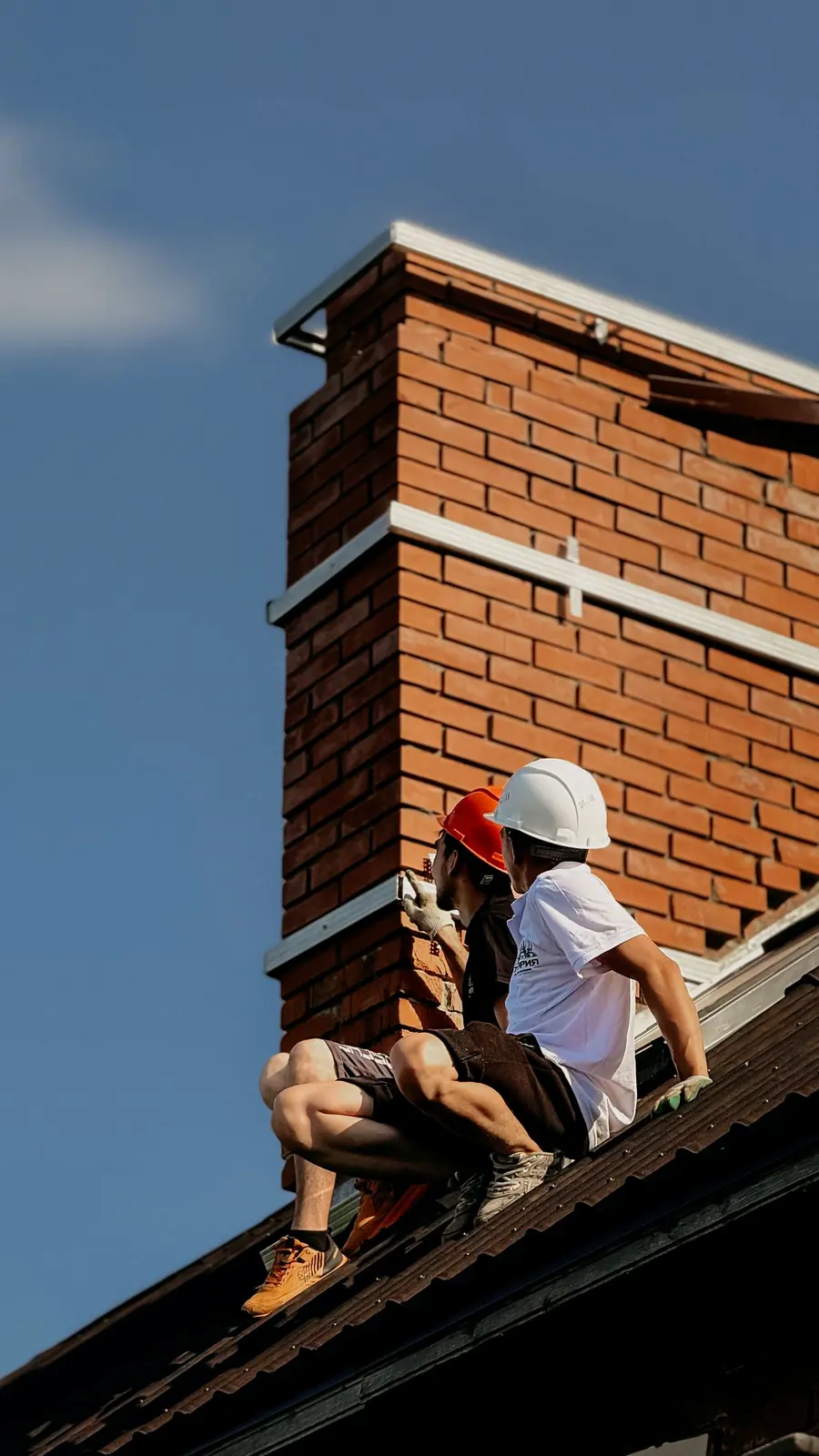 Two chimney technicians in hard hats repointing the brickwork of a chimney stack